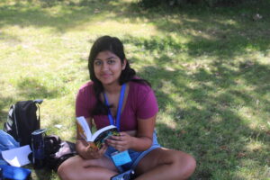 teen girl sitting in grass reading a book at summer camp